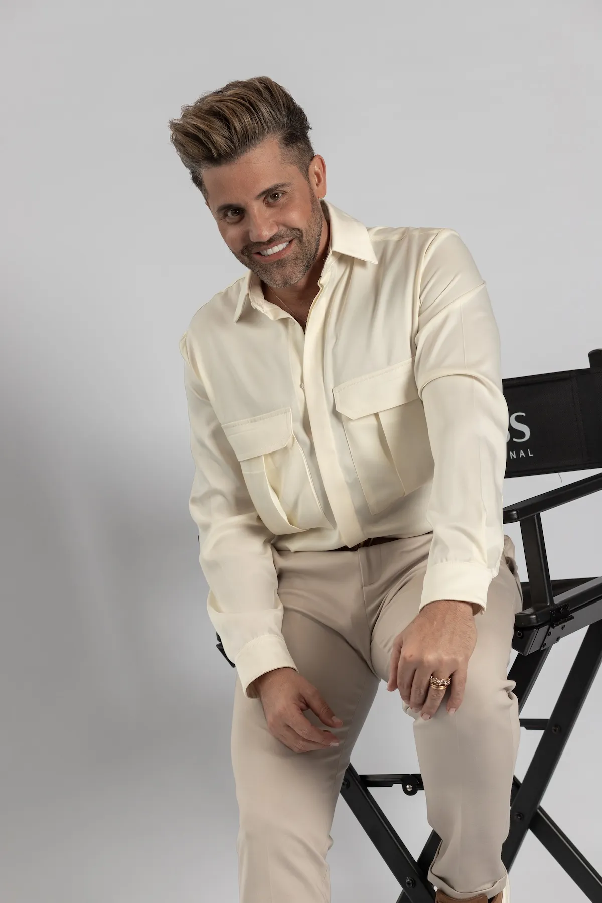 Gabriel Samra sonriendo, apoyado en una silla, con camisa crema